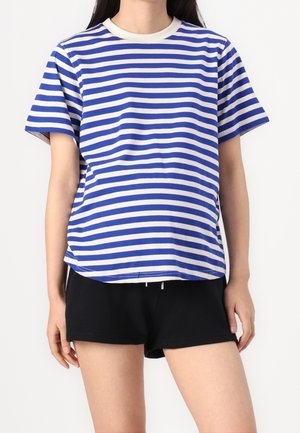 T-shirt rayé bleu et blanc en coton, avec des manches courtes et un col rond. Porté avec un short noir, légèrement ample.