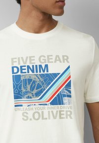 Biała bawełniana koszulka z graficznym wzorem w niebieskie, czerwone i jasnoniebieskie paski oraz napisem: "FIVE GEAR DENIM UNLEASH YOUR INNER DRIVE."