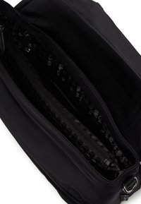 Borsa in tessuto nero con una fodera interna testurizzata, scomparti con zip e un'esterno liscio. Include un logo circolare e dettagli metallici.