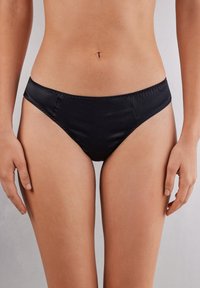 Czarne satynowe majtki bikini o niskim stanie, z gładką teksturą i subtelnymi detalami przeszycia wzdłuż krawędzi.