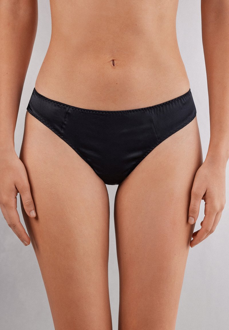 Czarne satynowe majtki bikini o niskim stanie, z gładką teksturą i subtelnymi detalami przeszycia wzdłuż krawędzi.