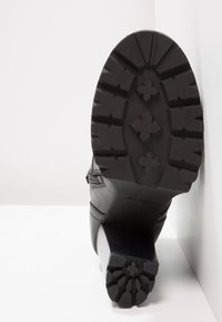 Botín negro hasta el tobillo con parte superior de cuero liso, suela texturizada y un patrón de taco audaz. Presenta un pequeño tacón y detalles de costura.