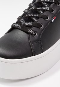 Černé kožené tenisky s bílou texturovanou platformou, s černými šňůrkami s bílým textem a malou logovou akcentací.