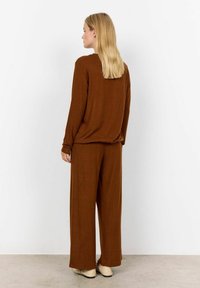 Top en tricot marron et pantalon large assorti. Texture douce, coupe décontractée, manches longues et silhouette ample. Chaussures de couleur claire.
