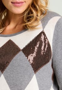 Suéter de punto con un patrón de diamantes en gris y crema, con un detalle de diamante marrón adornado con lentejuelas en el frente.