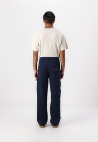 Navy cargo pants with multiple pockets and a relaxed fit, paired with a light beige crew neck t-shirt, shown from the back.
