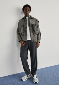 Gray oversized shirt with two large pockets, white T-shirt underneath, gray tailored pants, and silver athletic shoes with black accents.
