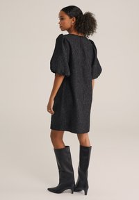 Rochie neagră texturată cu mâneci bufante, cu o siluetă până la genunchi. Asortată cu cizme negre cu toc până la genunchi, punând în evidență un look modern și elegant.