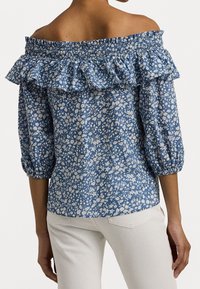 Modrá květinová blůza s odkrytými rameny, řaseným výstřihem, nadýchanými rukávy a elastickými manžetami, s bílým květinovým vzorem na strukturované tkanině.