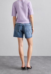 Lawendowy, dziergany top z krótkim rękawem o fakturowanym wzorze, w połączeniu z ciemnoniebieskimi szortami jeansowymi. Całość dopełniają czarne sandały na obcasie.