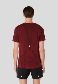 Maron atletisk skjorte med struktureret design og logo, med rund halsudskæring og korte ærmer, parret med sorte shorts.
