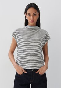 Top corto a maniche corte in bianco e nero con un collo alto. Presenta un motivo a griglia e una vestibilità rilassata, abbinato a jeans di denim scuri.