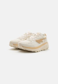 Beige and cream athletic shoes made of mesh and suede, featuring a padded collar, textured sole, and subtle tan accents.