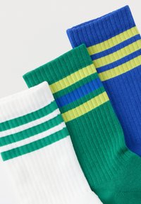 Τρία ζευγάρια ριμπ κάλτσες: λευκές με πράσινες ρίγες, πράσινες με μπλε και κίτρινες ρίγες, και μπλε με πράσινες και κίτρινες ρίγες.