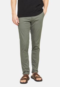 Pantalons en coton slim fit de couleur olive avec des poignets roulés, associés à des sandales plates marron avec deux brides et une semelle large.
