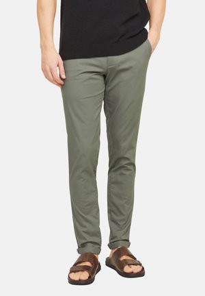 Pantalones de algodón verde oliva ajustados con puños enrollados, combinados con sandalias planas marrones con doble tira y suela ancha.