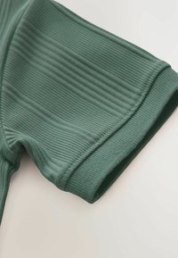 Grøn ribbet stof med en struktureret overflade. Ærmet har et glat fold og rene kanter, der understreger dets strømlinede design.