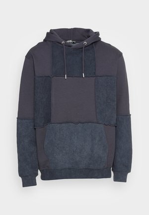 Sudadera con capucha que presenta un diseño de patchwork en diferentes tonos de azul oscuro y marino, fabricada con una suave tela texturizada y con cordones ajustables.