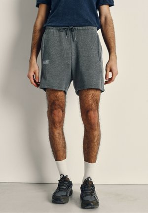 Gray athletic shorts with a textured fabric, elastic waistband, drawstring, and side pockets, paired with black sneakers and white socks.