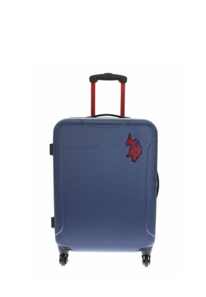 Valise rigide bleue avec poignée télescopique rouge, quatre roues et un patch rouge représentant un joueur de polo dans le coin supérieur droit.