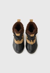 Braune und schwarze Winterstiefel mit einer strukturierten Sohle, einem pelzigen Innenfutter und gepunkteten Schnürsenkeln, von oben auf einem weißen Hintergrund betrachtet.