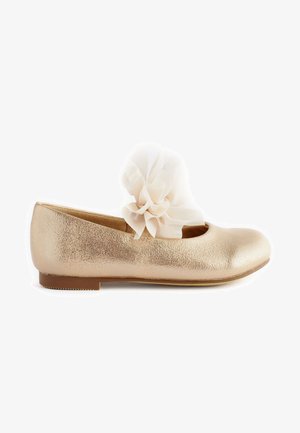 Kultaiset ballerinat, joissa on teksturoitu pinta, pyöristetty kärki ja suuri kermaisen värinen organza kukka koristeena hihnassa. Tasapohja.