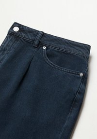 Jean en denim bleu foncé avec poche avant, passants pour ceinture et détails en bouton et rivet argentés sur un fond clair.