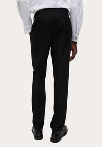 Czarne formalne spodnie o dopasowanym kroju, z płaskim przodem i bocznymi kieszeniami, w połączeniu z czarnymi butami i białą koszulą z długim rękawem.