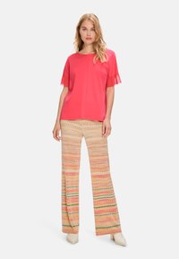 Red short-sleeve top with frilled edges and straight-cut patterned pants featuring zigzag designs in pink, yellow, and green tones.