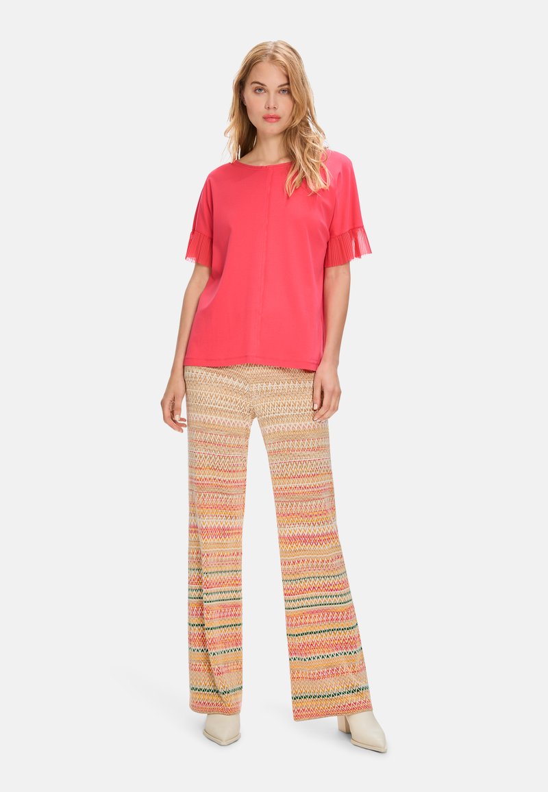 Red short-sleeve top with frilled edges and straight-cut patterned pants featuring zigzag designs in pink, yellow, and green tones.