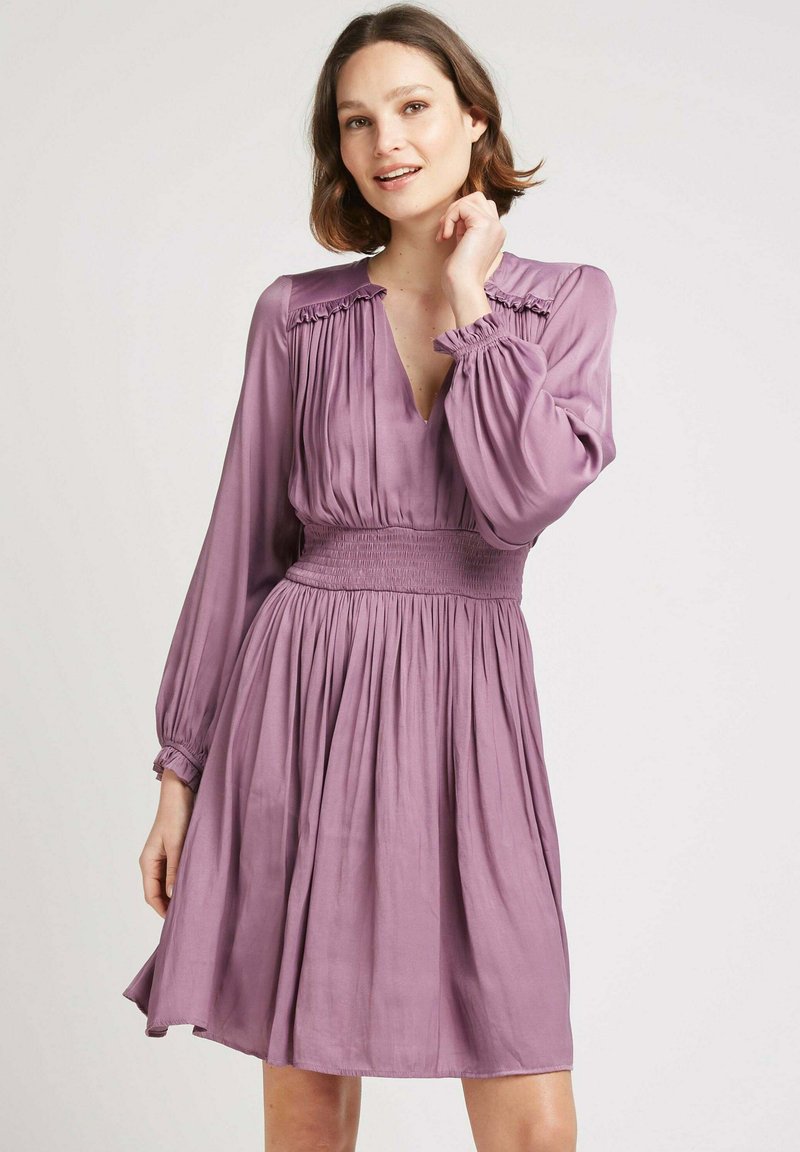 Robe lavande à manches longues, taille smockée et décolleté en V. Présente un design plissé et des accents froncés au niveau des épaules. Texture de tissu douce.