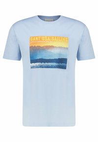 Camiseta de algodón azul claro con un estampado gráfico que presenta montañas y agua, acentuado por el texto "GANT USA SAILING" en la parte superior.
