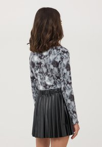 Maglietta a maniche lunghe con un motivo a marmo grigio e nero abbinata a una gonna plissettata in ecopelle nera con vita alta. Tessuto morbido e design aderente.