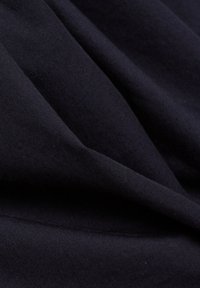Tissu bleu marine foncé avec une texture de tissage visible, plié pour créer des ombres douces, superposées et des plis légers.