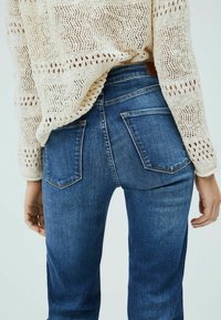 Jeans i denim i medelblå färg med rak benpassform. Har en mid-rise midja, två bakfickor och en texturerad krämfärgad stickad tröja ovanpå.