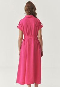 Rosa bomulds midi-kjole med korte, rullede ærmer, krave og belted talje. Let faldende nederdel med en kant, der rammer midt på læggen.