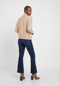 Maglione beige a maglia con colletto alto, abbinato a jeans a zampa d'elefante blu scuro e stivaletti alla caviglia in pelle con stampa serpente marrone. Tessuto morbido e vestibilità rilassata.