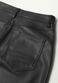 Pantalon en fausse cuir noir montrant le haut du dos avec une poche cousue et des passants de ceinture sur un fond plat clair.