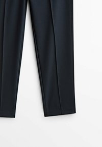 Pantalons ajustés bleu foncé avec une texture lisse, présentant un design à jambe droite et des plis le long de l'avant.
