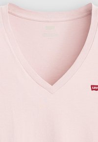 T-shirt rose clair en col en V fabriqué en coton avec une texture douce. Présente un petit logo rouge Levi's brodé sur le côté gauche.