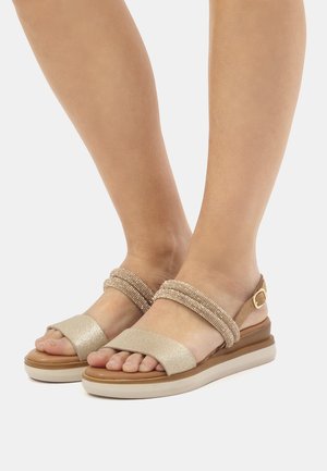 Gold-toned sandals feature textured straps with beaded accents, a wide front band, and a cushioned sole. Adjustable ankle strap present.