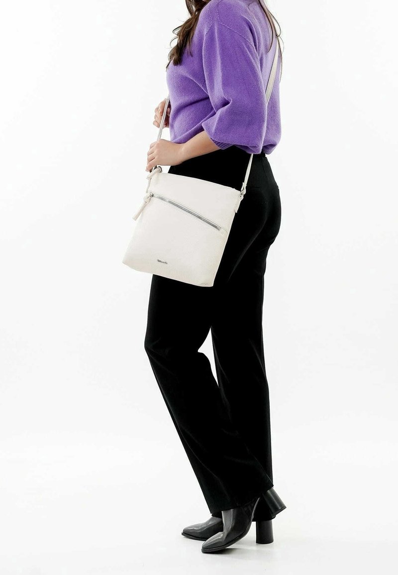 Borsa a tracolla bianca in pelle con tasca frontale con zip, texture liscia e tracolla regolabile, indossata da una persona con pantaloni neri.