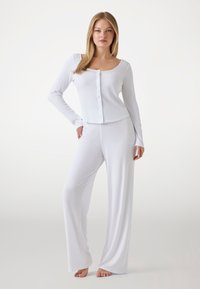 Witte lange mouwen overhemd gecombineerd met witte, luchtige broek. Zachte, comfortabele stof met een gladde textuur en een relaxte pasvorm.