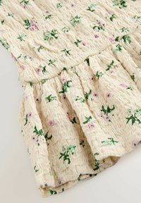 Tissu crème avec une texture froissée, orné de broderies florales vertes et roses, avec des détails froncés au bas.