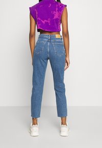 Jeans de mezclilla azul con corte recto y dobladillo deshilachado, que cuentan con dos bolsillos traseros. Combinados con un top corto de tintado en morado.