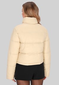 Kraftig pufferjakke i lys beige med høj krave, quiltet design og brede ærmer. Glat tekstur uden synlige dekorationer.