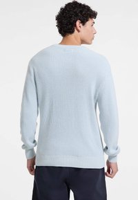 Pull en maille bleu clair avec texture en côtes, à manches longues et encolure ronde, présentant une coupe décontractée et des poignets roulés.