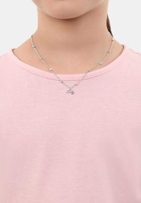 Collar de cadena de plata con cuentas de colores, que presenta un pequeño charm de arcoíris y estrella. Llevado sobre una camiseta rosa clara.