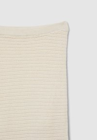 Tissu en tricot beige avec un tissage lâche et ouvert et un bord supérieur en côtes. La texture est douce, avec un motif homogène.