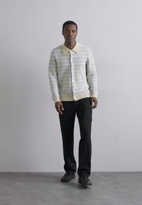 Pruhovaný cardigan v jasných barvách se žlutým límcem, kombinovaný s černými kalhotami. Jednoduchý design, texturovaná tkanina, zapínání na knoflíky.